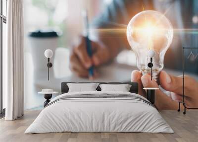 Innovation through ideas and inspiration ideas. Human hand holding light bulb to illuminate, idea of creativity and inspiration concept of sustainable business development. Wall mural