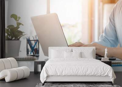 young man using laptop computer and mobile phone When looking for financial information in business, work at the desk. Writing with a pen, studying remotely from home and working from home. Wall mural