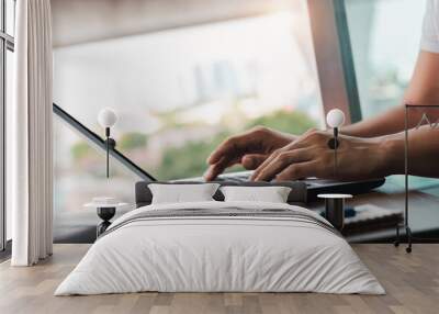 young man using laptop computer and mobile phone When looking for financial information in business, work at the desk. Writing with a pen, studying remotely from home and working from home. Wall mural