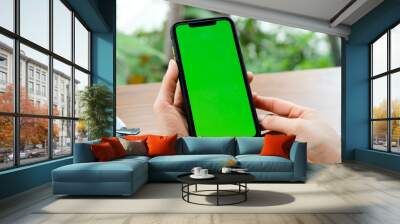 Mockup image of a business people holding smart mobile phone with blank green screen on vintage wooden table in modern cafe restaurant during meeting or lunch. Wall mural