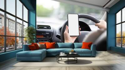 A woman driving a black car on a highway road. Hand holding a white touch screen mobile phone. Smartphone concept for text input and copy specs. Wall mural