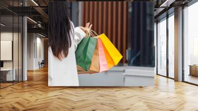 Asian woman holding shopping paper bags in a shopping mall and happy after shopping for her needs during the festival. Paper bags containing many products are in the hands of Asian woman. Wall mural