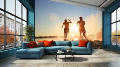 Glückliche junge Menschen laufen und springen am See beim Sonnenuntergang Wall mural