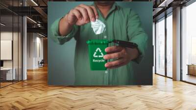 Man wearing a green shirt holding recycling bin and throw the paper in the bin, Waste sorting and sustainability concept, Recycle, Sustainable living and environmentally friendly habits concept. Wall mural