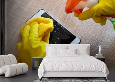 Female hand in rubber protective glove with rag wiping smartphone using cleaning spray. Wall mural