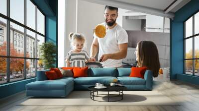 bearded happy father showing tricks with pancakes in the kitchen, close up photo. Wall mural