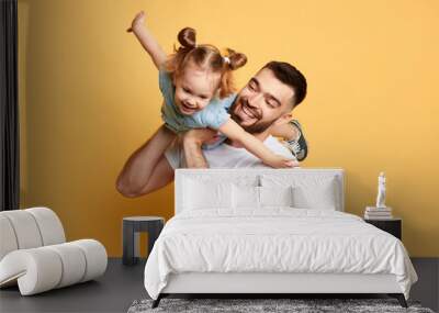 cheerful happy man teaching sweet lovely daughter to fly like a plane. close up photo. isolated yellow background. studio shot, happy moments with best father Wall mural