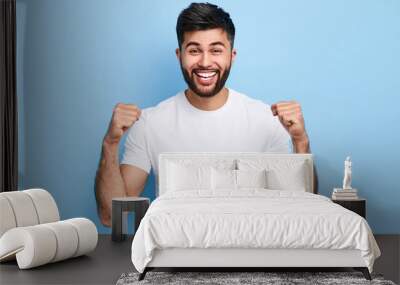 excited Arab man celebrating success with two fists in air isolated on the blue background. close up portrait, studio shot , happiness, positive emotion and feeling. I've done it. facial expression Wall mural