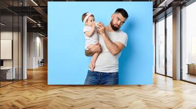 exhausted , tired father feeding his baby girl with milk bottle. close up photo. isolated blue background. studio shot. poor dad is fed up loking after child. Wall mural