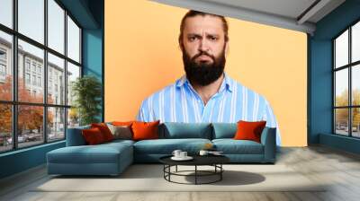 Nervous doubtful handsome bearded man in stylish shirt frowning his eyebrow, having puzzled look going to make serious decision.isolated yellow backgroun. studio shot Wall mural