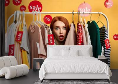 surprised girl hiding among clothes on hangers woman is being surprised after hearing the prizes of clothes. unbelievable sale. trade. close up photo. Wall mural