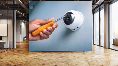 A hand using a screwdriver to install a security camera on a wall. Wall mural