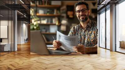 A portrait of a cheerful male financial advisor holding a finance report in his hand and sitting in front of a laptop at a wooden desk at home : Generative AI Wall mural