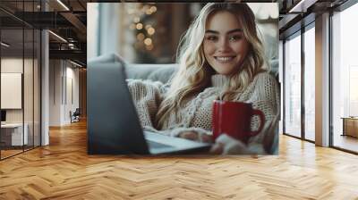 A woman is sitting on a couch with a laptop and a red coffee mug She is smiling and she is enjoying her time : Generative AI Wall mural