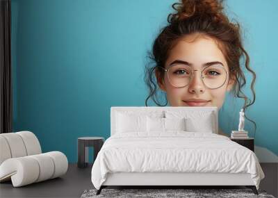 Attractive female student with curly hair wears transparent glasses white t shirt stands against blue background has calm face expression tender smile listens interlocutor with pleasur : Generative AI Wall mural