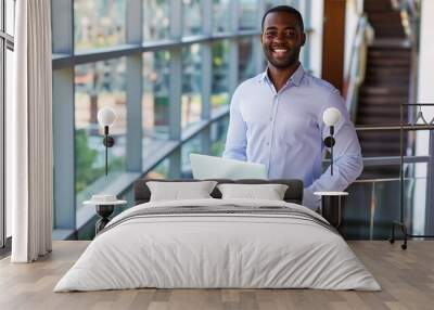 Confident business person in business casual attire stands on an office balcony With a smile he holds a laptop and looks directly at the camera representing success and creativity in t : Generative AI Wall mural