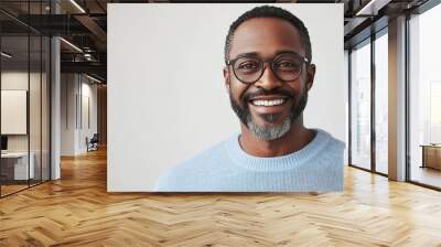 Middle aged cheerful dark skinned male with shining smile wears light blue sweater round spectacles achieves everything by himself stands against white studio wall has relaxed face exp : Generative AI Wall mural