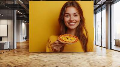 Photo of satisfied woman holds piece of pizza feels pleased as spends free time with friends in pizzeria looks happily directly at camera wears casual outfit isolated over yellow wall  : Generative AI Wall mural