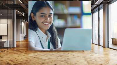 Portrait of a beautiful young and intelligentlooking Indian Asian woman student wearing a white shirt and green tracker smiling as she works on her laptop in a university classroom : Generative AI Wall mural