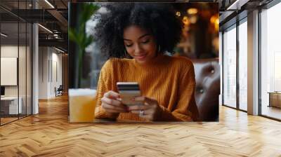 Shot of beautiful glad young female with Afro hairdo types number of credit card on smart phone makes purchase online or checks bank account recreats in outdoor cozy cafe with fresh co : Generative AI Wall mural