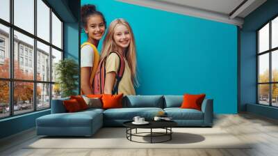 Two smiling young girls with backpacks pose against blue background Wall mural