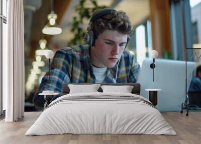 A young man in casual work attire and headphones focuses intently on his work at a laptop, taking notes in an office setting, Generative AI Wall mural