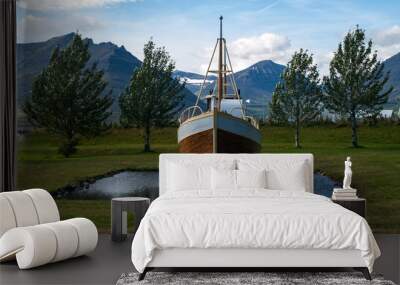 One boat levitating on a small lake surrounded with green grass, some trees and mountains and blue sky in the background. Iceland, Europe. Wall mural