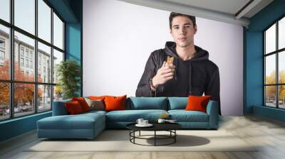 Handsome young man holding the cereal bar he's eating Wall mural