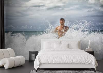 Handsome young man standing on a beach in Phuket Island, Thailand, getting hit by big wave's splash Wall mural