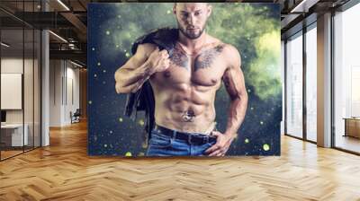 Muscular young man standing and looking to a side, shirtless, wearing jeans, showing chiselled torso, abs and pecs Wall mural