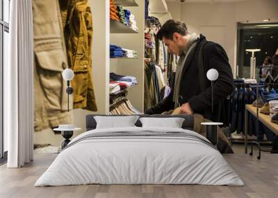 Side view of young male customer choosing shirt in menswear shop Wall mural