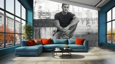 Young man sitting on dirty wall, looking at camera Wall mural