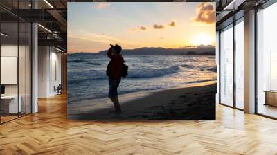 Older woman looking out to sea and enjoying beautiful sunset on a beach. Wall mural