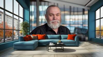 Portrait of a bearded middle-aged man. Happy senior man 50 55 60 years old with gray beard at the airport, office, indoors background looking at camera. Older man traveling concept Wall mural