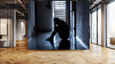 Silhouette of a sad young man sitting in the dark leaning against the wall with his back, The sun is in sorrow. Wall mural