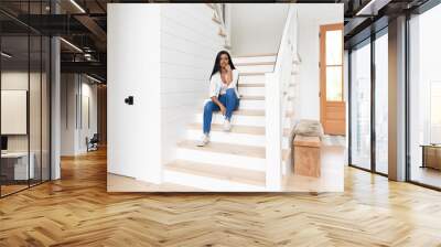 Indian woman sitting on the stairs of her modern brightly lit suburban home Wall mural