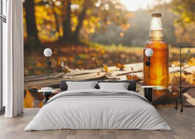 Bottle of filtered apple cider on a picnic table, surrounded by fallen autumn leaves and a clear sky Wall mural