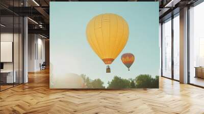 A bright yellow hot air balloon rising into the sky during a morning festival, surrounded by other colorful balloons. Wall mural