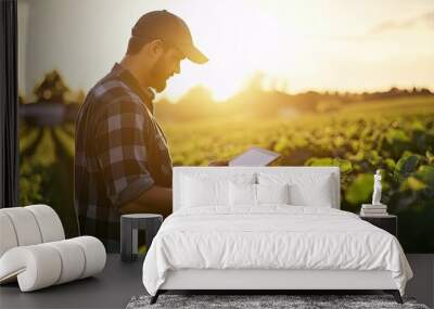 A professional agronomist using a digital tablet to assess the health of crops in a sunlit agricultural field. Wall mural