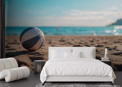 A volleyball in sharp focus on the sandy beach, surrounded by footprints, with the sea and sky softly blurred in the background. Wall mural