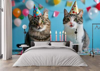 Birthday celebration with two cats, party hats on and a cake with candles, joyful blue background Wall mural