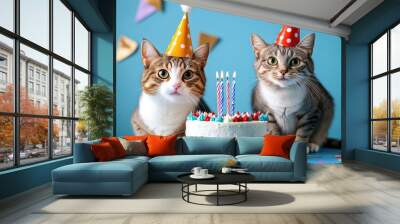 Birthday celebration with two cats, party hats on and a cake with candles, joyful blue background Wall mural