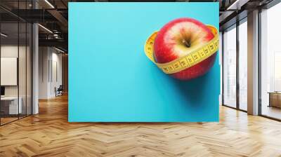 Crisp red apple wrapped with a yellow measuring tape on a clean blue background, emphasizing weight loss and nutrition concepts. Wall mural