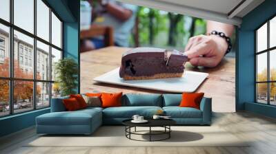 Cutting piece of rich chocolate tart cake with spoon served in white plate on wooden table. Selective focus. Wall mural