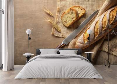 A fresh loaf of bread with a few slices, a knife, and wheat stalks on a burlap cloth Wall mural