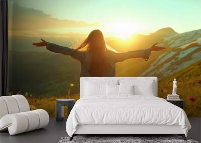 A female stands with her arms outstretched joyfully enjoying the sunrise amidst the majestic mountains.
 Wall mural