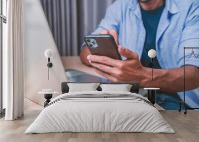 A man sitting in home and using mobile phone and laptop computer.  Wall mural