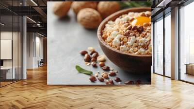 Wooden bowl filled with grains, nuts, and a cracked egg, surrounded by loose nuts and herbs on a table Wall mural