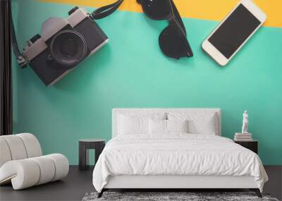 Flat lay design of work desk with sunglasses old camera and smartphone on green and yellow background. Wall mural