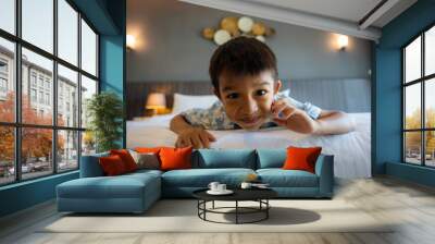 Little kindergarten boy enjoying play on white bed pillow hotel room Wall mural